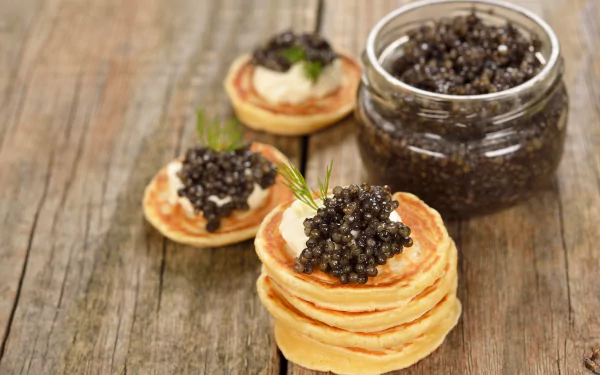 Mini pancakes topped with black caviar beside a jar on rustic wood — 5K Ultra HD PC desktop wallpaper and background (pancake, food, caviar).