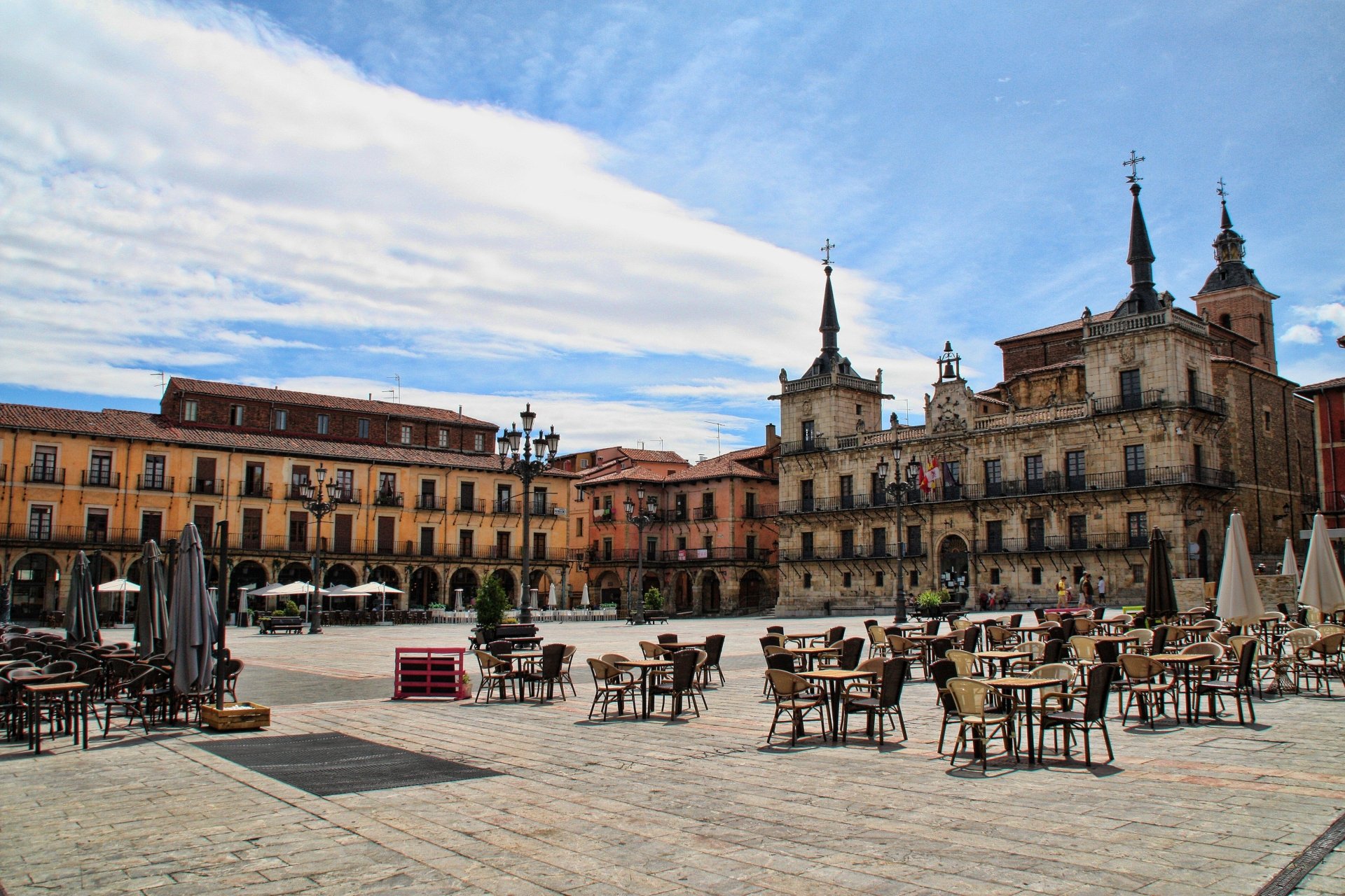 4K Ultra HD image of a historic town hall and surrounding square in Spain, featuring man-made buildings and outdoor seating under a partly cloudy sky.