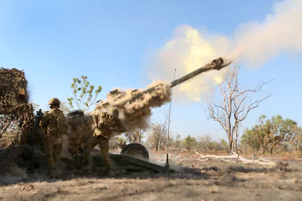 Soldier operating an M777 howitzer artillery in a dry, open landscape with smoke and dust from the firing, captured in 4K Ultra HD quality.