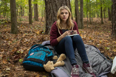 Chloë Grace Moretz sits on a sleeping bag in a forest, holding a bowl, in a scene from the movie The 5th Wave. The image serves as a 4K Ultra HD wallpaper.