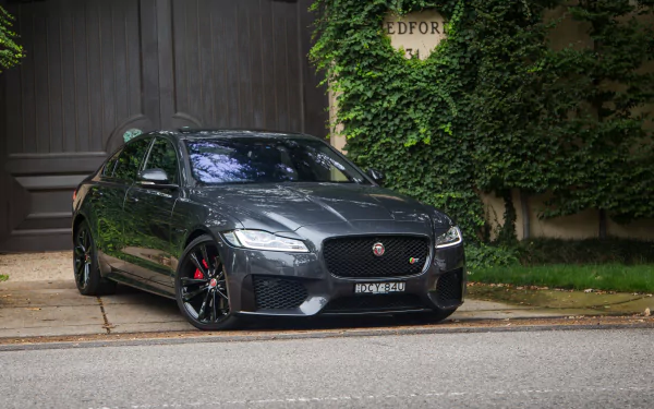 A sleek silver Jaguar XF parked on a quiet street with greenery and a wooden gate in the background, showcased as an HD PC desktop wallpaper.