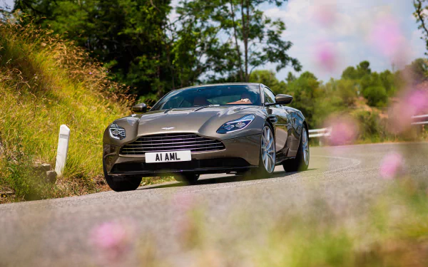 A silver Aston Martin DB11 grand tourer car driving on a scenic road, captured in stunning 4K Ultra HD as a PC desktop wallpaper and background.