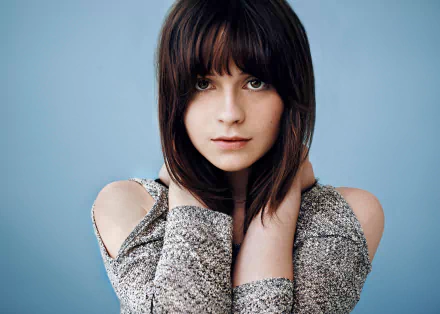 Close-up HD portrait of English singer Gabrielle Aplin with brunette hair and brown eyes against a soft blue background, suitable as a PC desktop wallpaper.