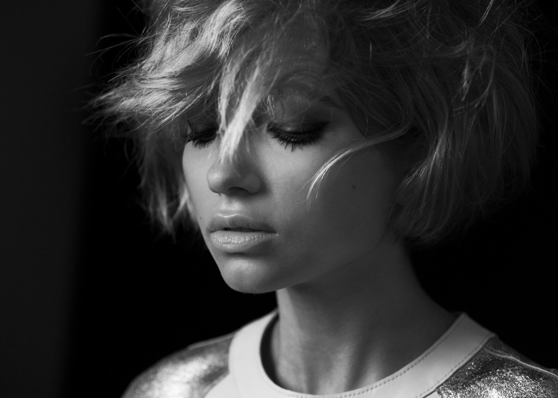 Black-and-white HD desktop wallpaper: close-up portrait of an American woman with short tousled hair, soft lighting, and a contemplative, downward gaze.