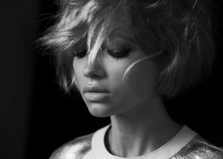 Black-and-white HD desktop wallpaper: close-up portrait of an American woman with short tousled hair, soft lighting, and a contemplative, downward gaze.