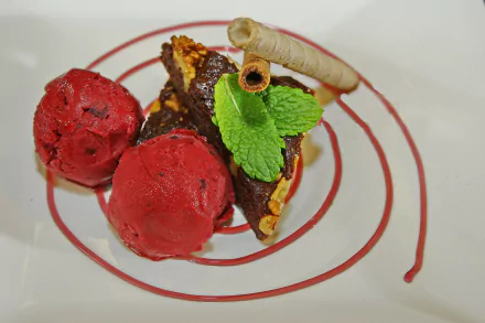 A vibrant dessert plate featuring red ice cream scoops, a biscuit topped with mint leaves and a rolled wafer, artfully presented on a white plate with a spiral sauce design in 4K Ultra HD.