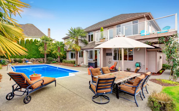 4K Ultra HD wallpaper showing a modern house with a spacious patio featuring cushioned chairs, a dining table, and a man-made pool surrounded by tropical plants.
