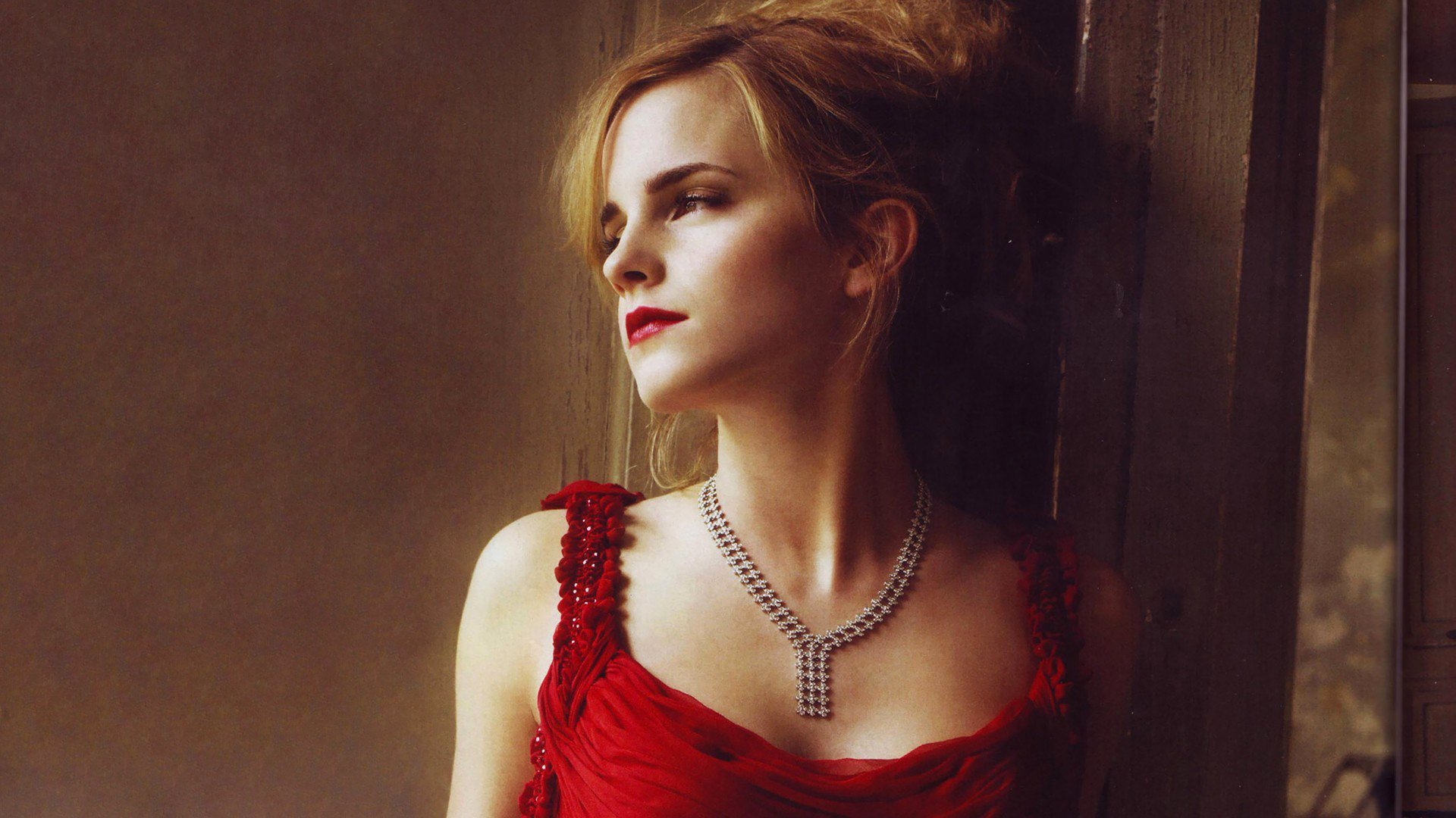 HD PC desktop wallpaper featuring celebrity Emma Watson in a red dress, looking thoughtfully to the side against a muted background.