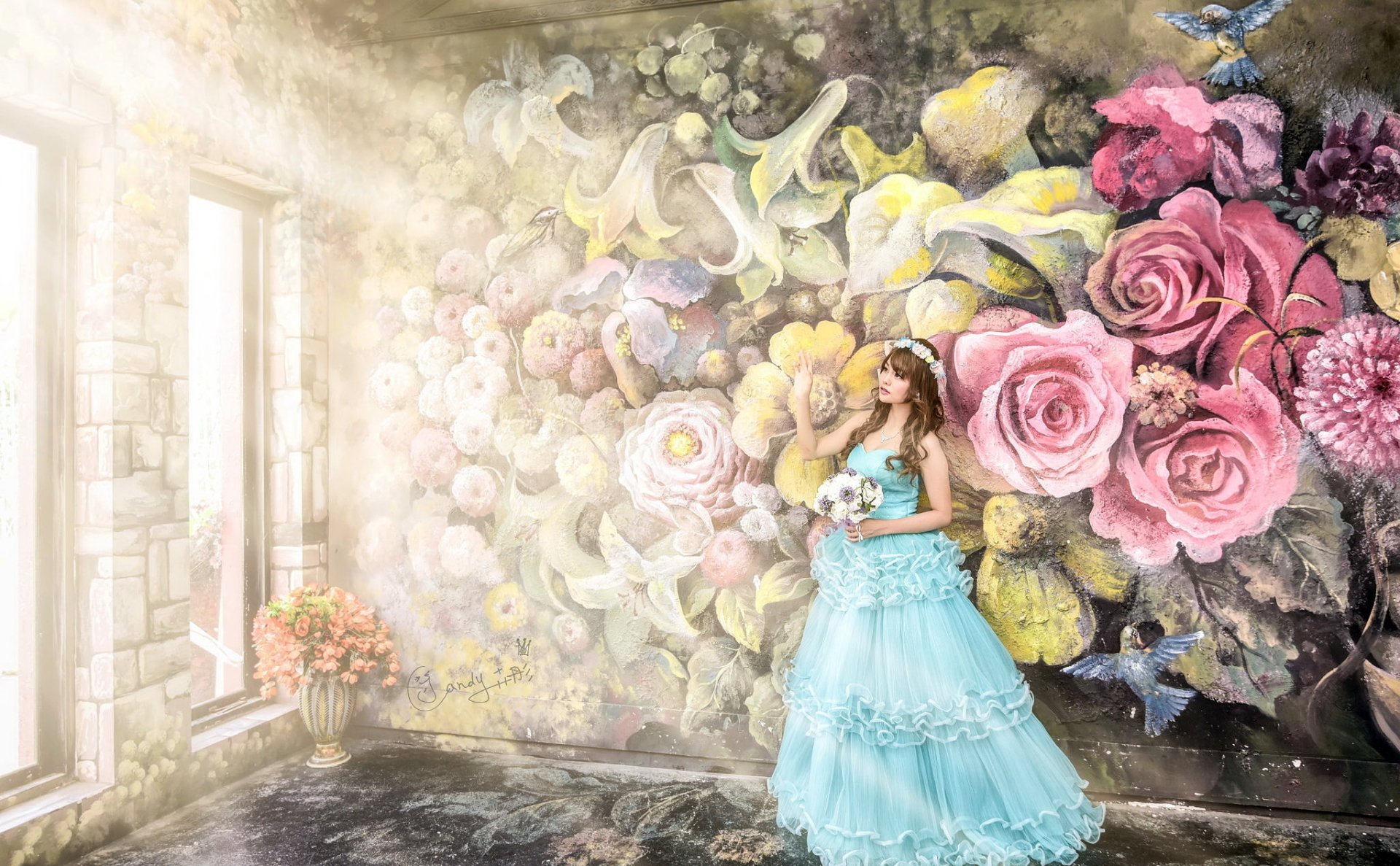 An Asian bride in a blue wedding dress stands in a sunlit room adorned with graffiti art of vibrant flowers.