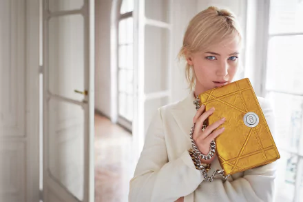 A stylish blonde actress poses with a yellow purse, showcasing her blue eyes. The elegant setting adds to the sophisticated vibe of this HD wallpaper.