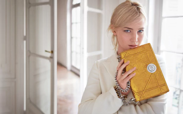 A stylish blonde actress poses with a yellow purse, showcasing her blue eyes. The elegant setting adds to the sophisticated vibe of this HD wallpaper.