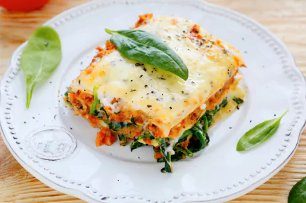 HD desktop wallpaper featuring a close-up of a cheesy lasagna slice garnished with fresh basil leaves on a white plate.