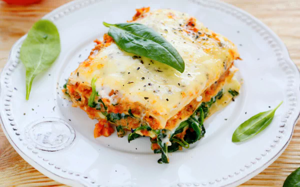 HD desktop wallpaper featuring a close-up of a cheesy lasagna slice garnished with fresh basil leaves on a white plate.