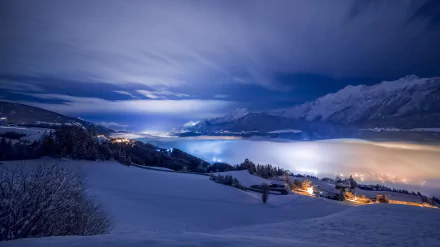 A serene winter landscape at night featuring a blue-toned mountain backdrop, a cozy house illuminated amidst the snow-covered terrain, creating a peaceful and scenic atmosphere.