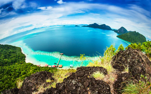 Fisheye 2K Quad HD PC desktop wallpaper/background of a curved coastline and turquoise ocean under a cloud-streaked sky, viewed from a rocky cliff toward distant islands on the horizon.