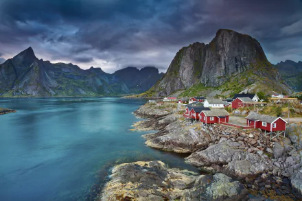A stunning mountain landscape in Reine, Norway, features vibrant red houses nestled along the rocky shoreline, against a backdrop of dramatic peaks and serene waters in Lofoten.
