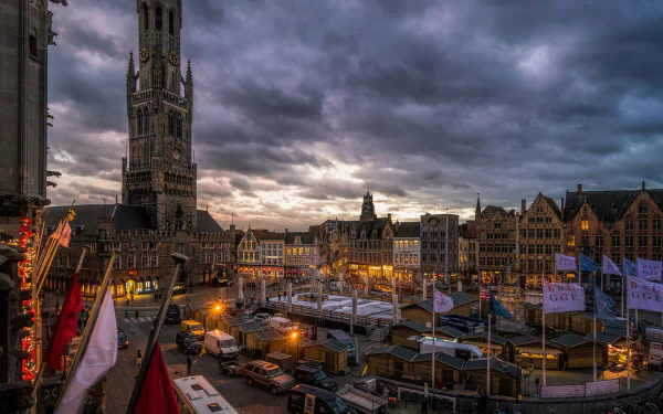 Dusk sets over Bruges, Belgium, highlighting the architectural beauty of the square and its buildings, with a striking tower in the background. A captivating city scene.
