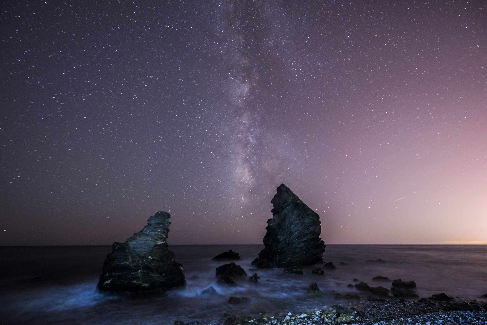 HD desktop wallpaper of a starry night sky with the Milky Way over an ocean horizon, featuring rocky formations and a serene sci-fi atmosphere.
