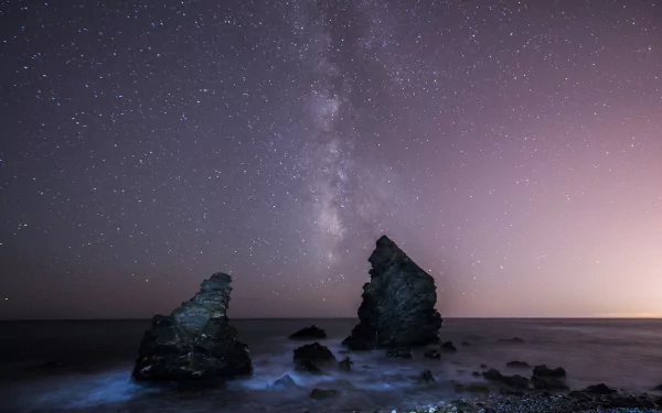 HD desktop wallpaper of a starry night sky with the Milky Way over an ocean horizon, featuring rocky formations and a serene sci-fi atmosphere.