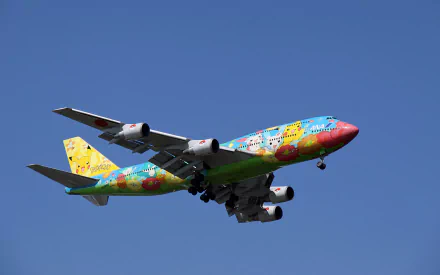 A colorful Boeing 747 airplane decorated with Pokémon characters soars against a clear blue sky, creating a vibrant and playful desktop wallpaper scene.
