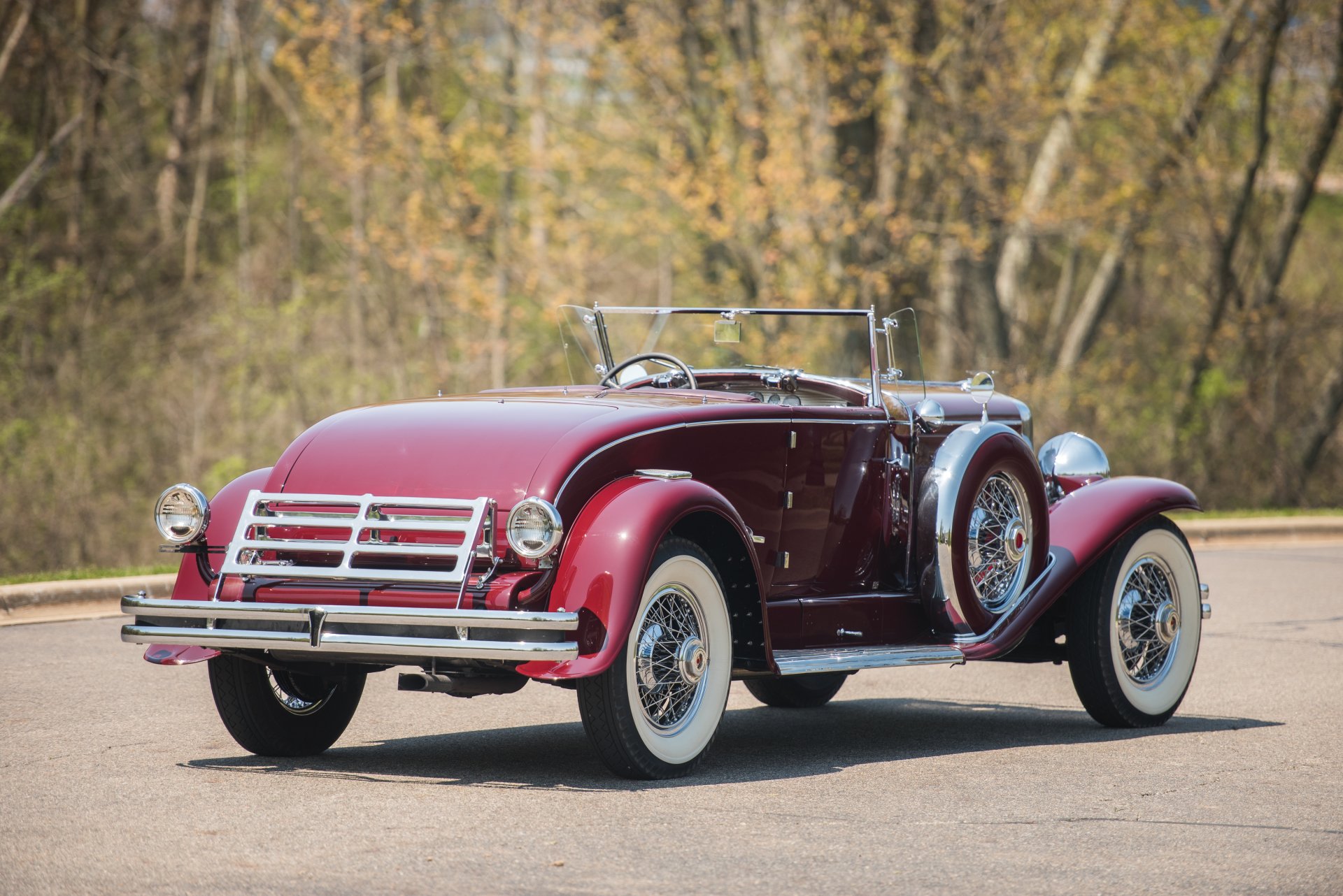 A vintage 1929 Duesenberg Model J Disappearing Top Convertible Coupe in deep red, showcased as an HD PC desktop wallpaper with a wooded background.