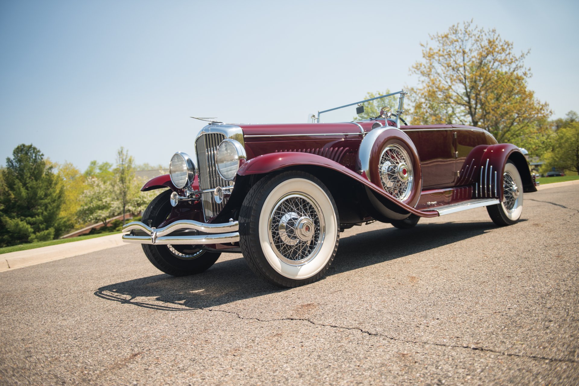 A vintage 1929 Duesenberg Model J Disappearing Top Convertible Coupe parked on a sunlit road, captured in high definition as a PC desktop wallpaper background.