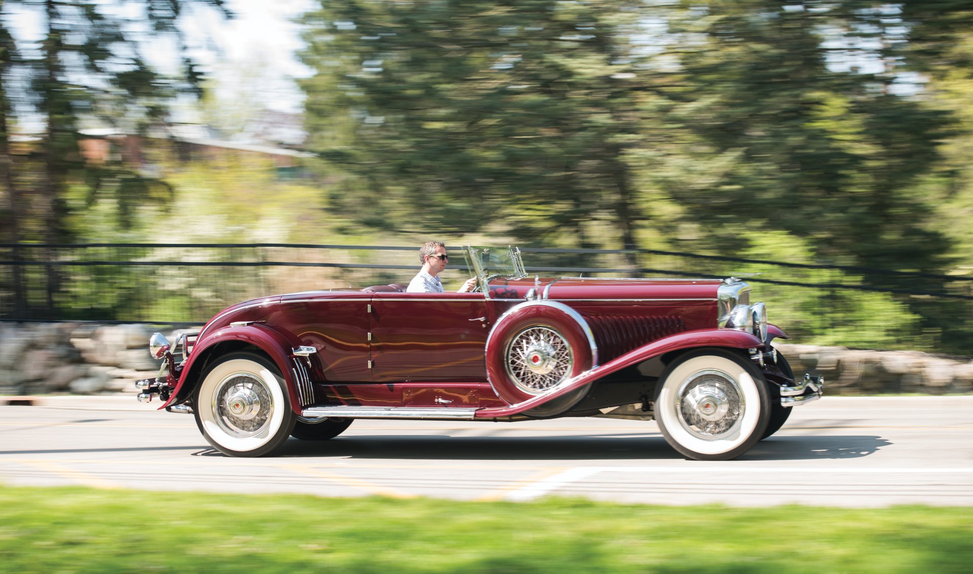 HD wallpaper of a vintage 1929 Duesenberg Model J Disappearing Top Convertible Coupe cruising on a road, showcasing classic automotive design and elegance.
