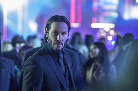 HD desktop wallpaper and background featuring Keanu Reeves as John Wick from the movie John Wick: Chapter 2. The image shows John Wick in a black suit amidst a vibrant, out-of-focus crowd.