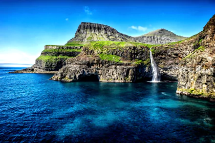 A stunning HD wallpaper depicting a Hawaiian coastline, featuring dramatic cliffs, a vibrant waterfall, and the serene blue ocean under a clear sky, showcasing the beauty of nature.