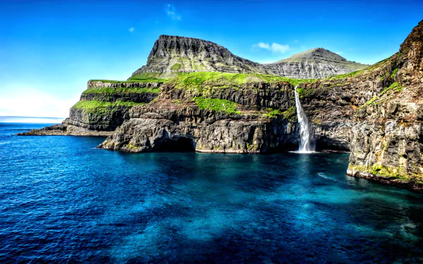 A stunning HD wallpaper depicting a Hawaiian coastline, featuring dramatic cliffs, a vibrant waterfall, and the serene blue ocean under a clear sky, showcasing the beauty of nature.