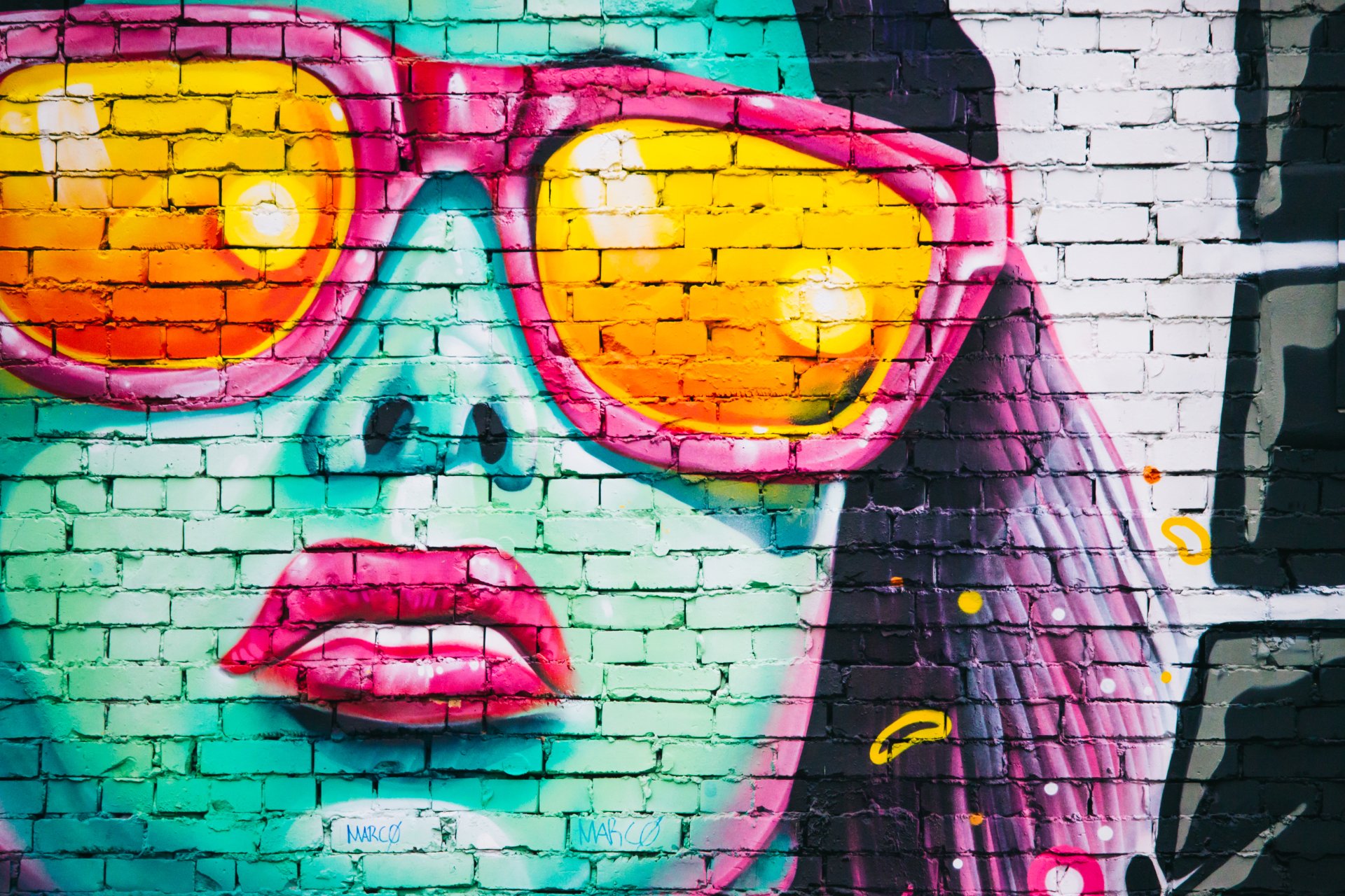 Artistic graffiti of a face with turquoise skin and bright pink sunglasses on a brick wall, captured in 4K Ultra HD for a vivid PC desktop background.
