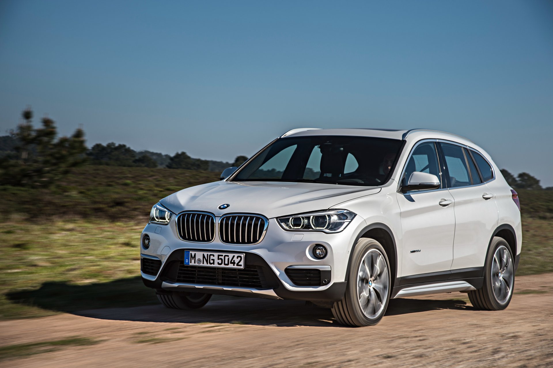 White BMW X1 SUV driving on a dirt road under a clear blue sky, captured in 4K Ultra HD as a PC desktop wallpaper and background.