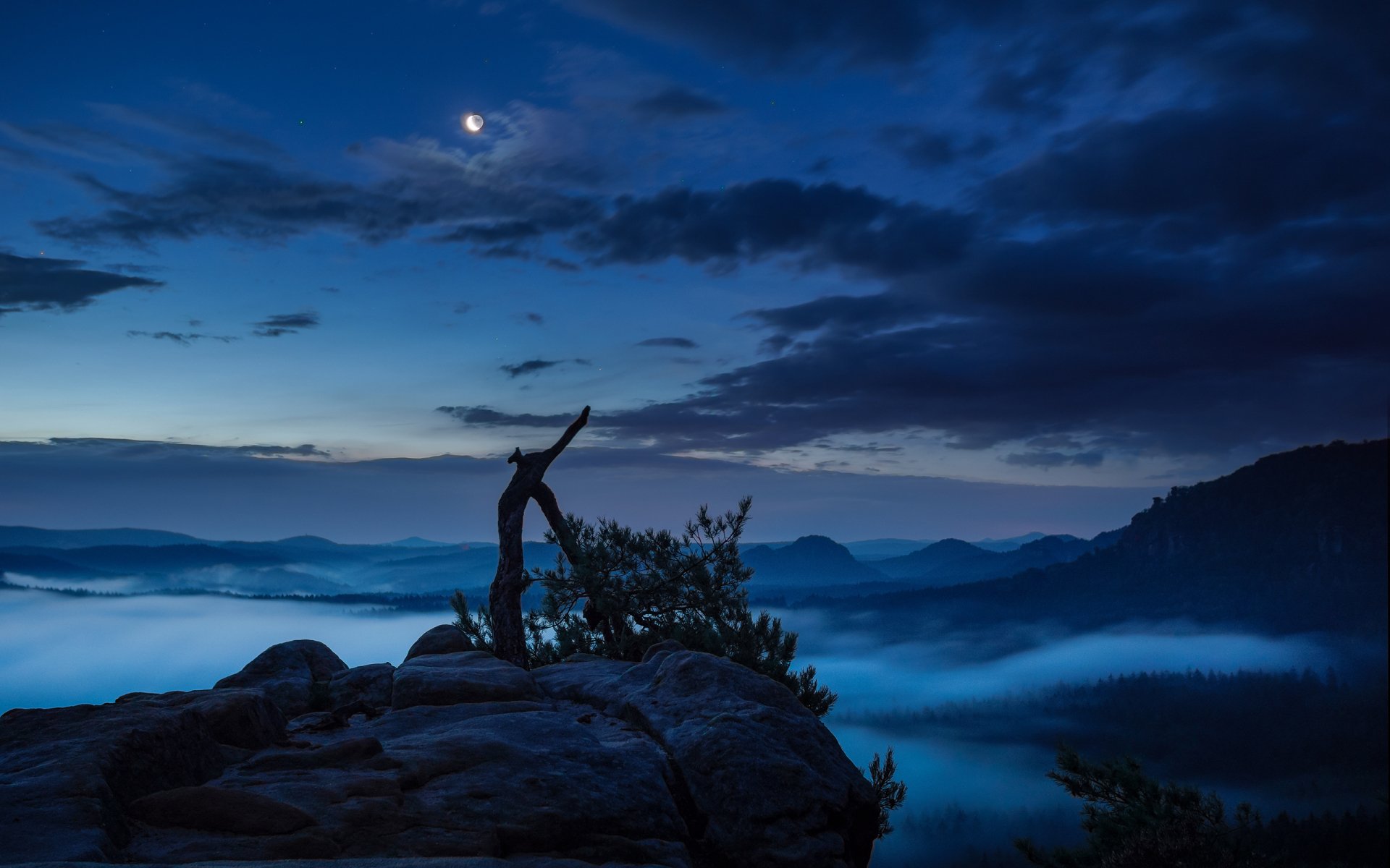 HD PC desktop wallpaper showing a foggy night sky with clouds, moon, and natural rocky landscape beneath.