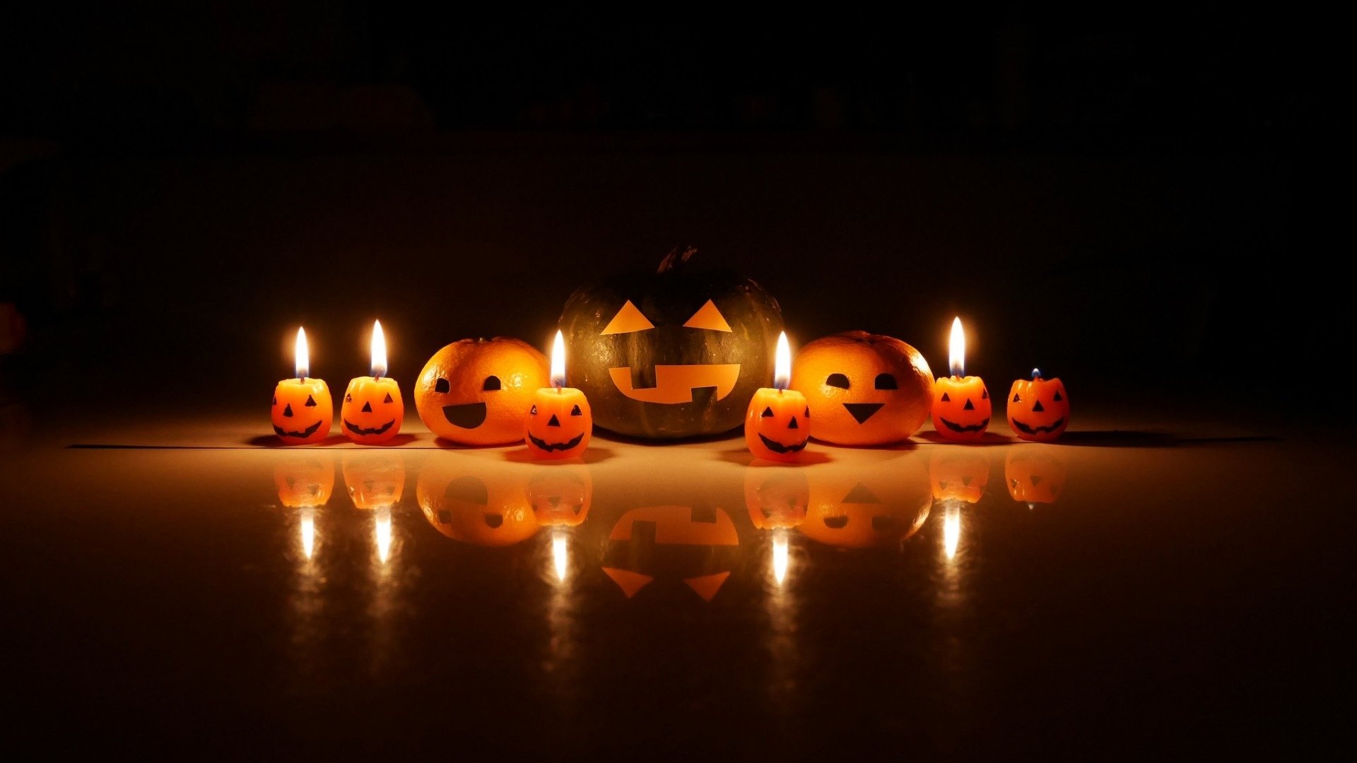 HD Halloween desktop wallpaper featuring a group of glowing jack-o'-lantern pumpkins illuminated by candlelight against a dark background.