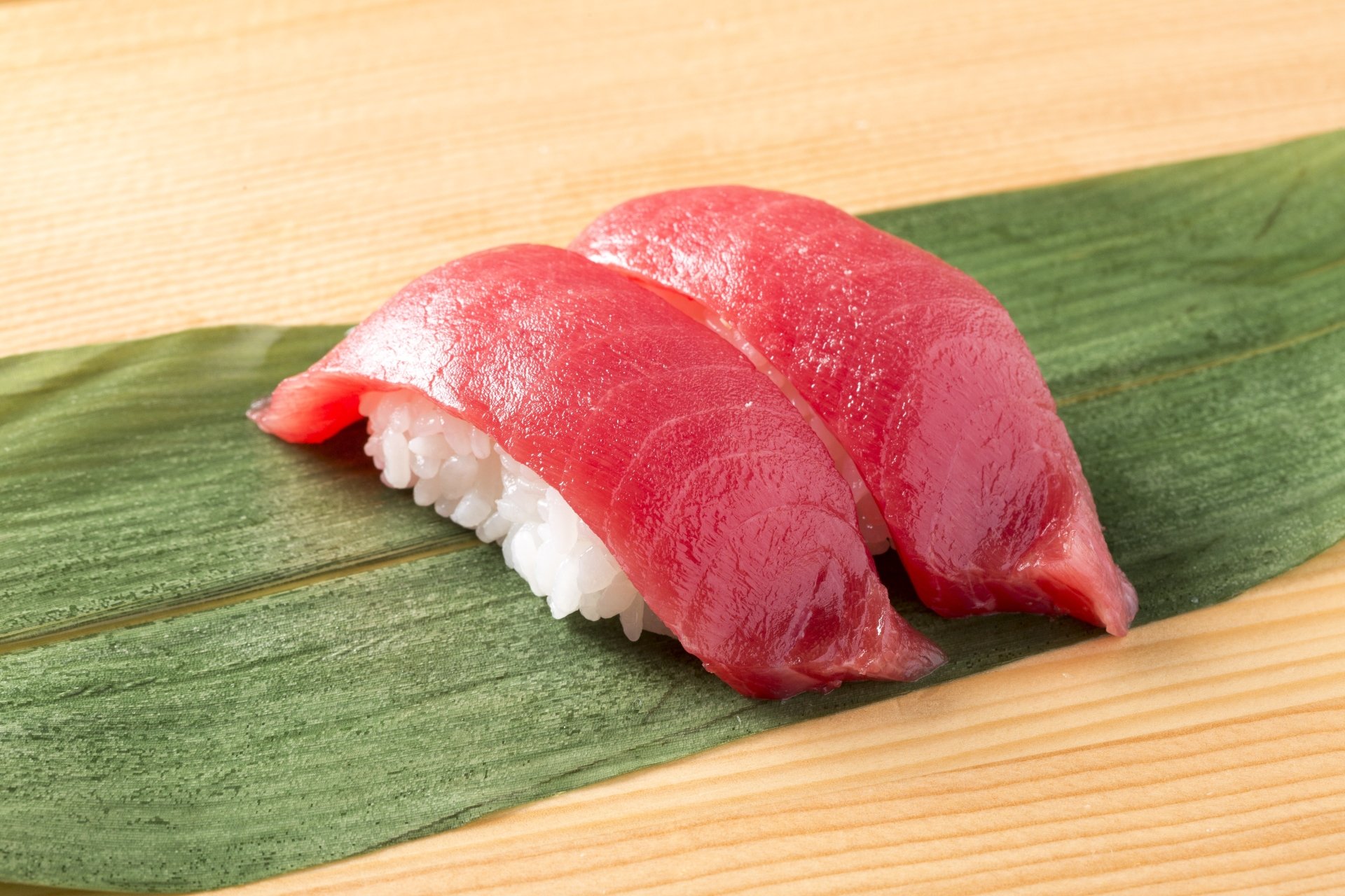 Close-up 4K Ultra HD wallpaper featuring two pieces of fresh fish sushi on rice, elegantly placed on a green leaf over a wooden surface.