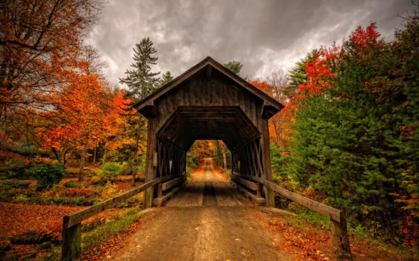 HD desktop wallpaper featuring a man-made covered bridge surrounded by vibrant fall trees under a cloudy sky.