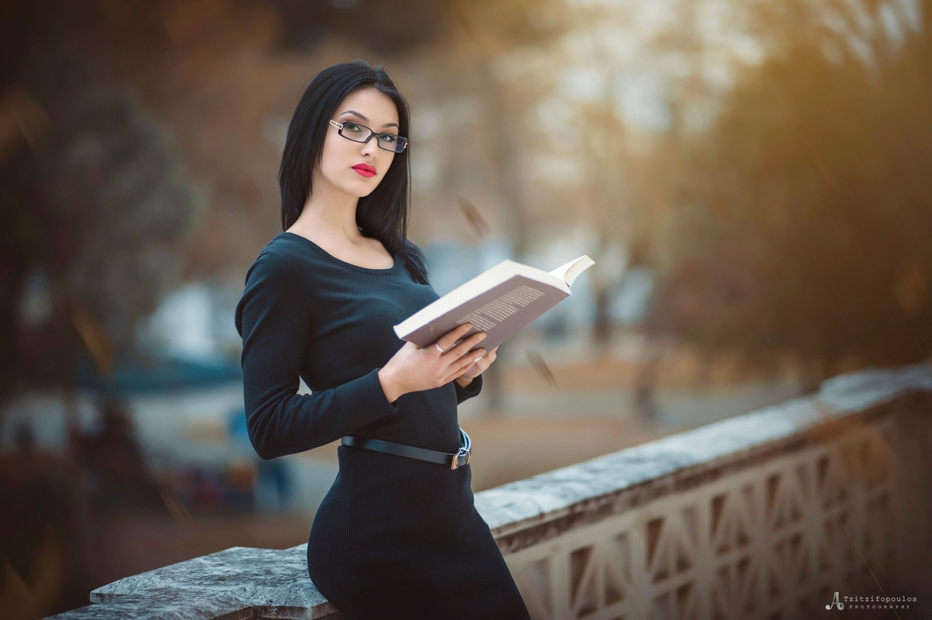A brunette woman with glasses and red lipstick poses with a book outdoors, featuring a beautiful depth of field. This HD image serves as an inspiring desktop wallpaper.