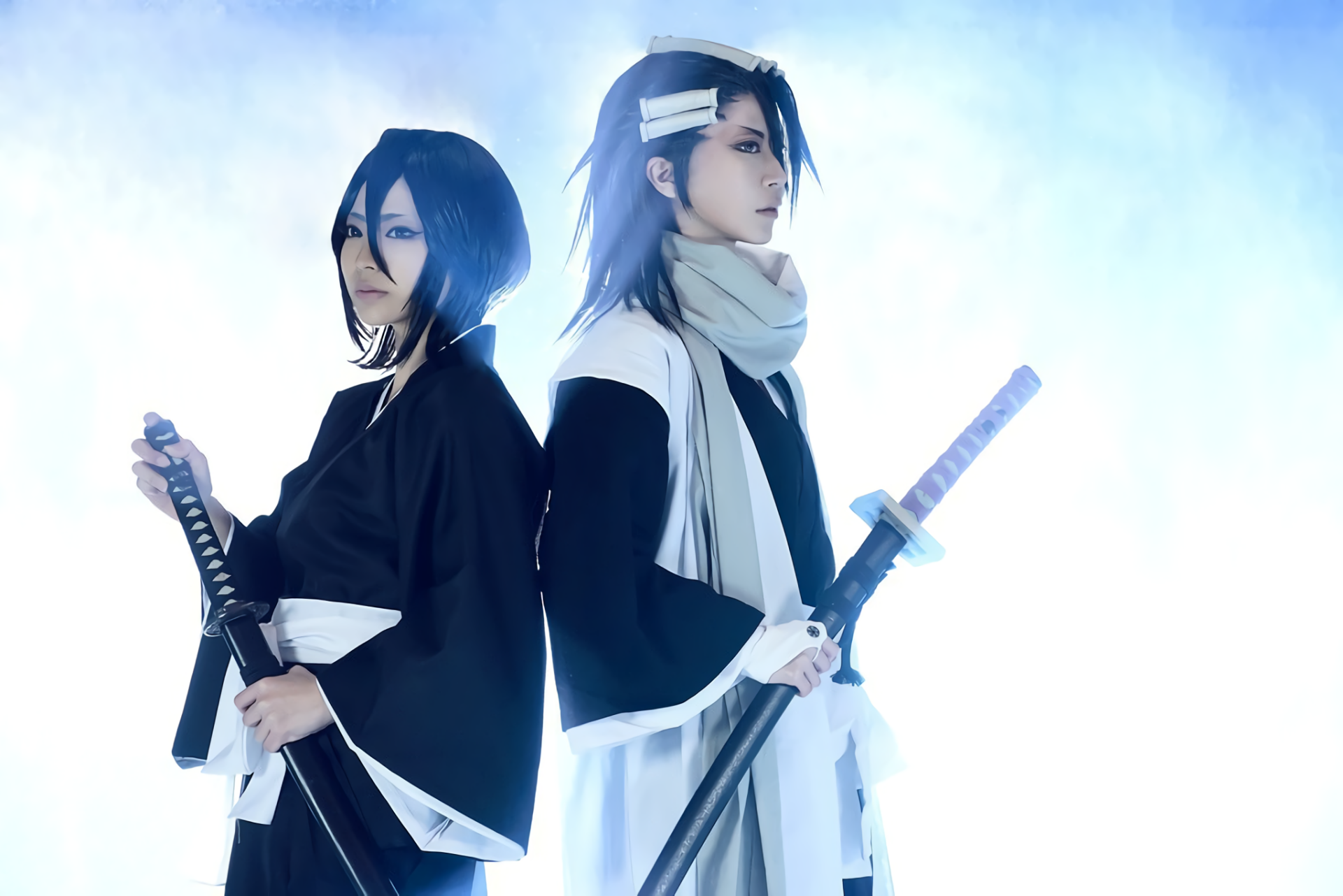 HD desktop wallpaper featuring women cosplaying as Byakuya Kuchiki and Rukia Kuchiki from Bleach, both holding swords against a light blue background.