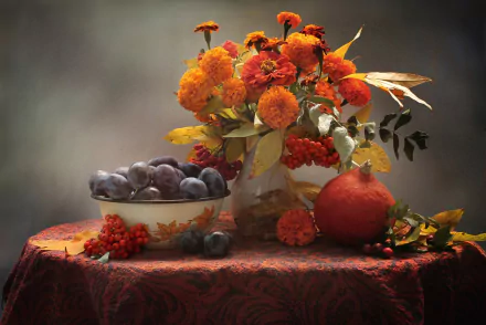 Still life HD wallpaper featuring vibrant orange marigold flowers, a small pumpkin, and a bowl of plums arranged on a richly textured tablecloth, evoking the colors of fall.