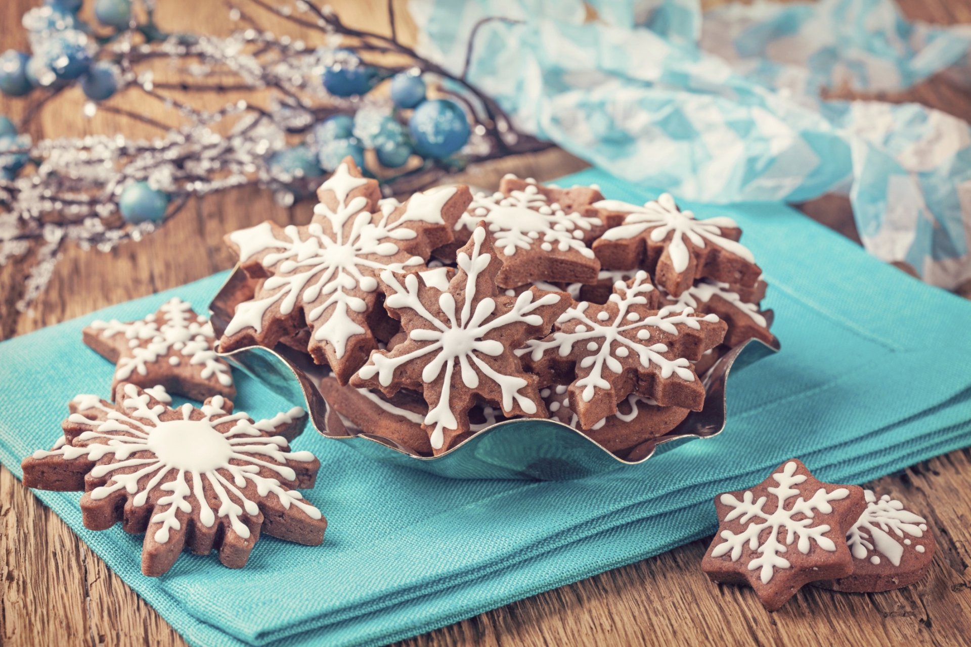 HD PC desktop wallpaper featuring festive chocolate cookies decorated with white snowflake icing on a wooden table with a blue cloth background.