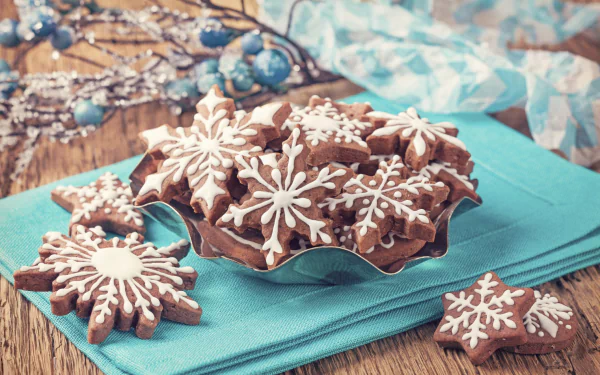 HD PC desktop wallpaper featuring festive chocolate cookies decorated with white snowflake icing on a wooden table with a blue cloth background.