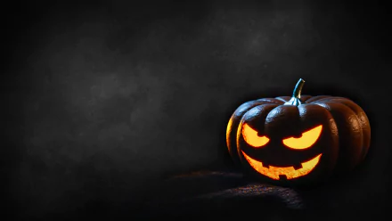 A glowing jack-o'-lantern with a sinister face illuminates a dark background, captured in 4K Ultra HD as a Halloween-themed PC desktop wallpaper.