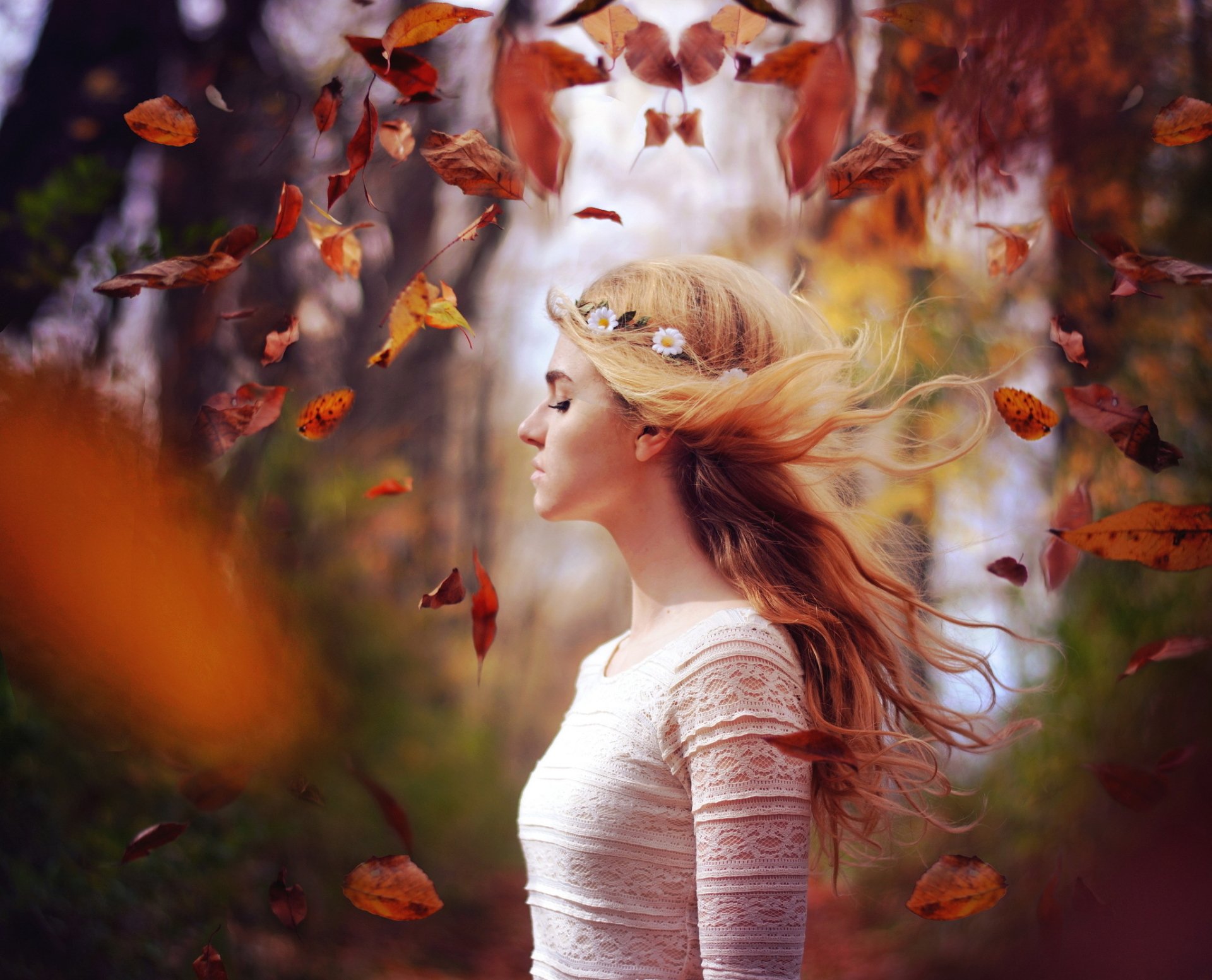 A blonde woman with flowing hair stands amidst swirling fall leaves, captured in a moody, shallow depth of field for an HD desktop wallpaper.