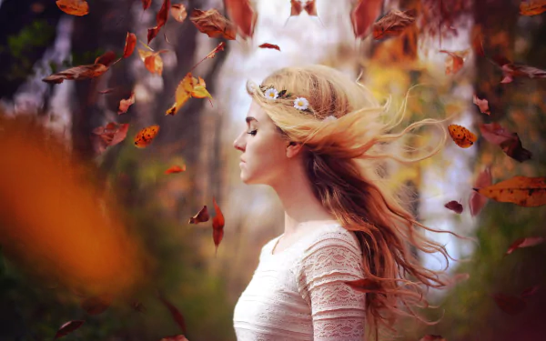A blonde woman with flowing hair stands amidst swirling fall leaves, captured in a moody, shallow depth of field for an HD desktop wallpaper.