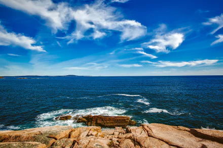 Maine HD PC desktop wallpaper — rocky coastline with foreground rocks, blue ocean and waves under a cloud-streaked sky meeting the distant horizon; a nature ocean background.