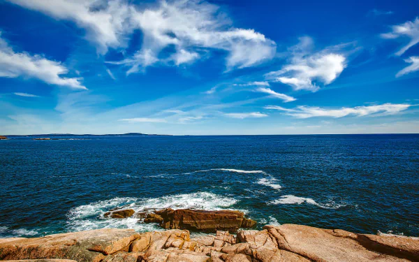 Maine HD PC desktop wallpaper — rocky coastline with foreground rocks, blue ocean and waves under a cloud-streaked sky meeting the distant horizon; a nature ocean background.