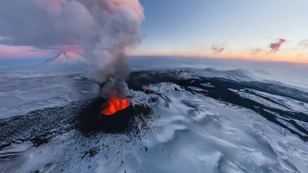 A stunning aerial view of a volcano erupting with glowing lava amidst a snowy, icy winter landscape, captured as an HD desktop wallpaper and background. Smoke billows into the sky, painting a dramatic scene.