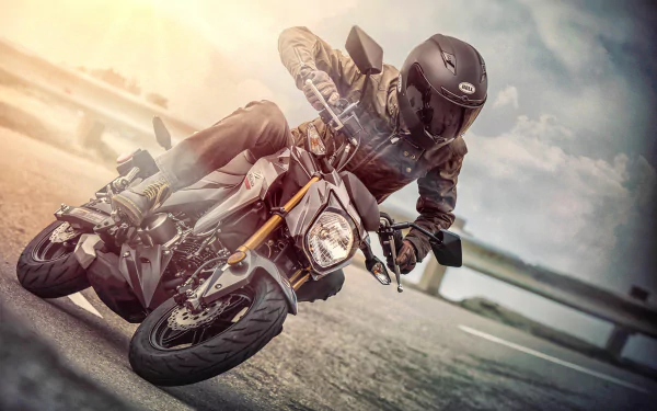 A rider leans into a turn on a Kawasaki Z125 Pro motorcycle, captured in dynamic motion against a blurred outdoor background. HD PC desktop wallpaper.