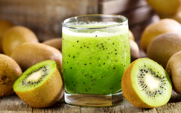 A vibrant glass of kiwi juice surrounded by whole and halved kiwifruit, captured in sharp detail as a 4K Ultra HD desktop background.