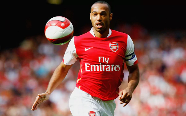 French soccer player in red Arsenal kit sprinting after a ball in a packed stadium — dynamic sports 2K Quad HD PC desktop wallpaper.